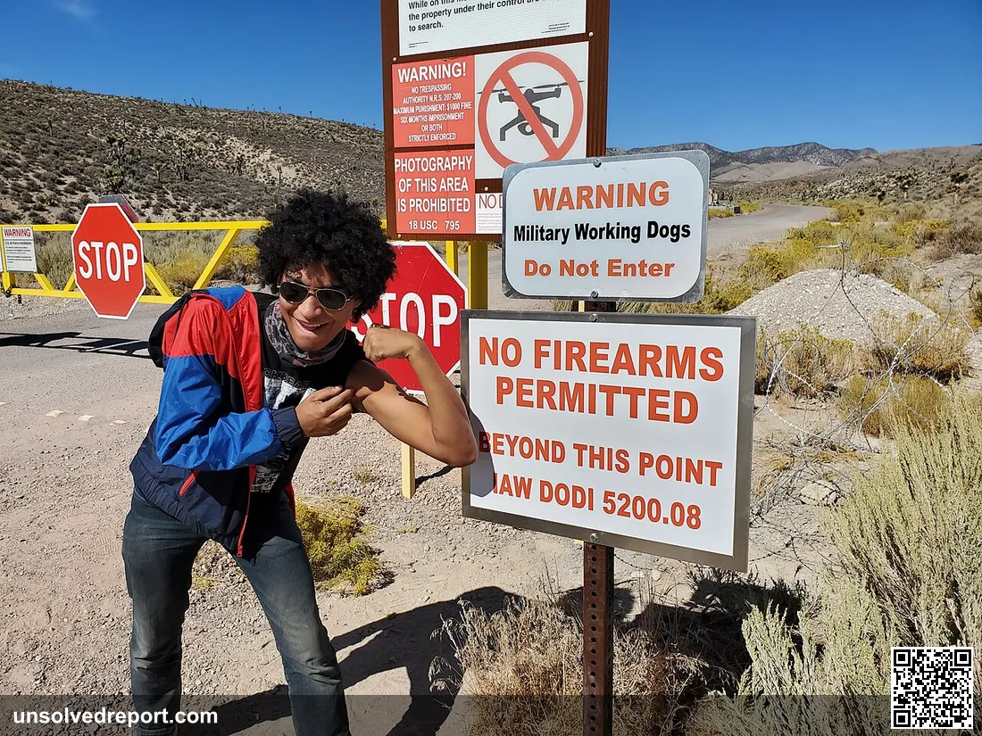 An attendee of Raid Area 51 posing in front of a No Firearms sign in front of the main gate of Area 51